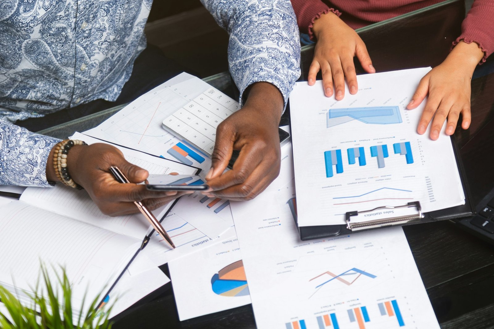 Hands of black people holding mobile phone on background of financial documents in business space